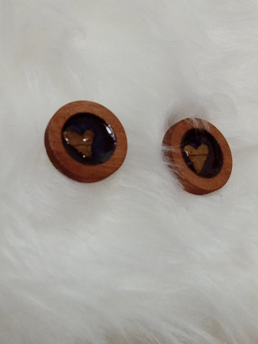 Handmade earrings on a wooden base with a piece of punched-out tree leaf